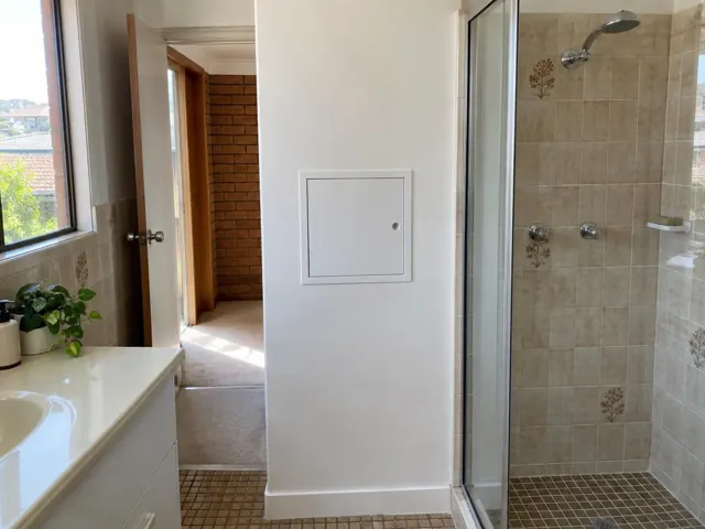 Bathroom wall with small access panel beside a shower and vanity in a tiled home in Sutherland